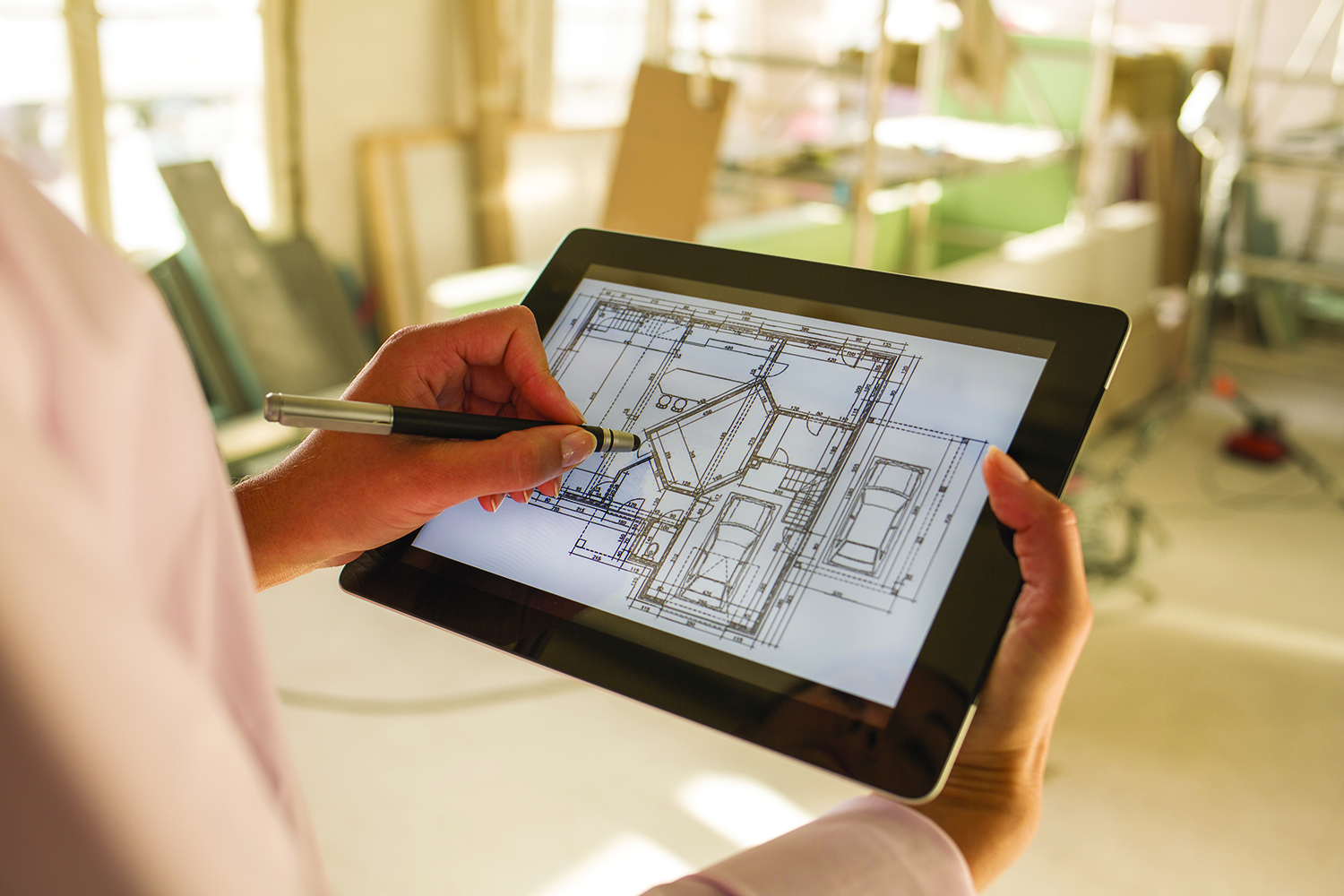 Person holding a tablet and marking a digital architectural floor plan at a construction site.
