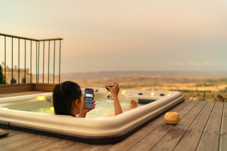 Woman in a rooftop hot tub with a glass of wine and smart home system on her phone. 